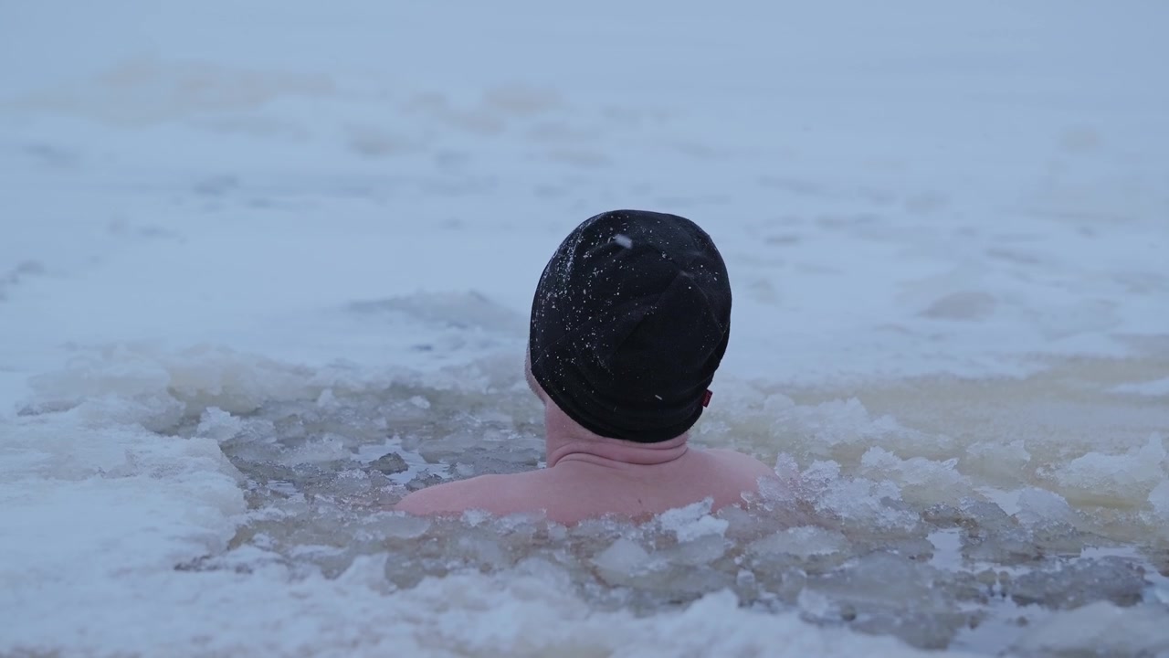 Close up of man immersed to shoulders in icy Daugava during snowfall, slow mo