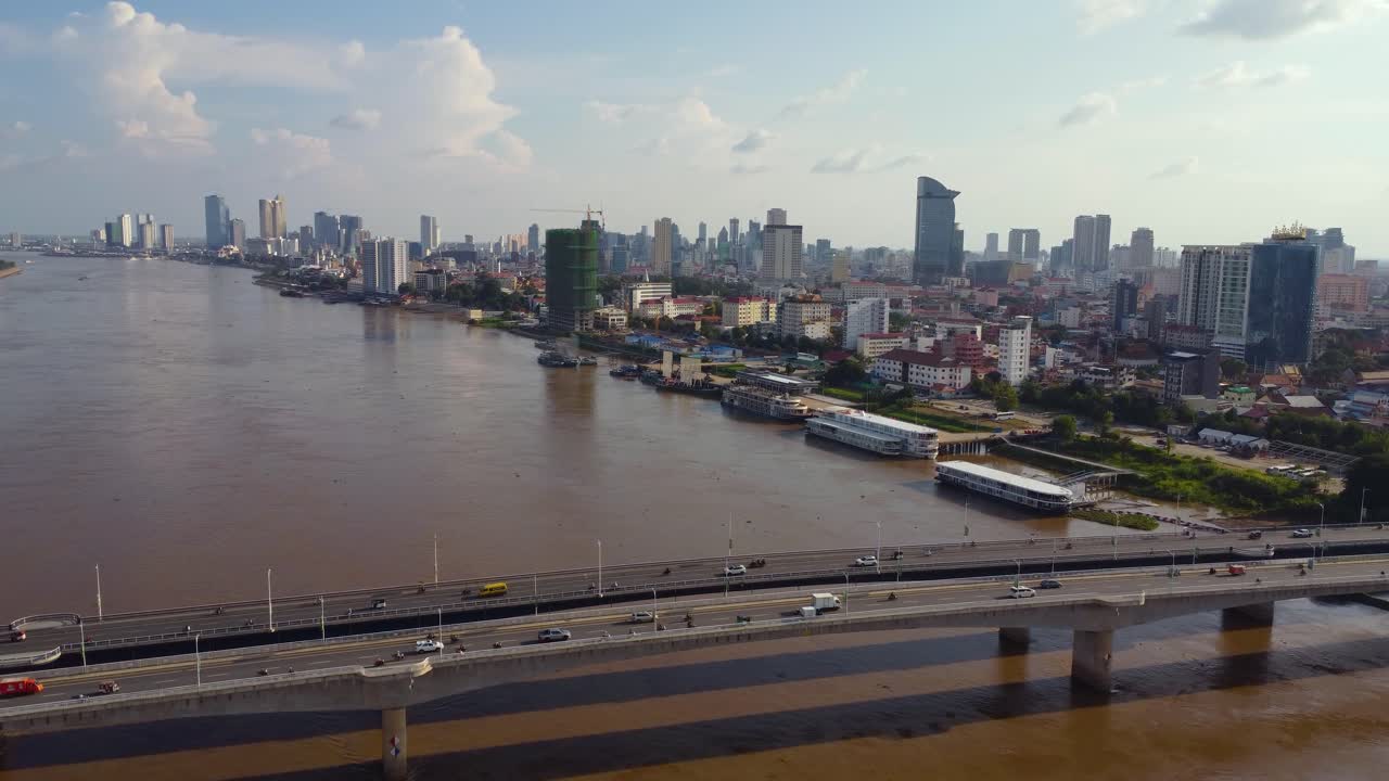 강 을 가로지르는 다리 를 지나가는 자동차 들 의 드론 뷰, 멀리 있는 도시