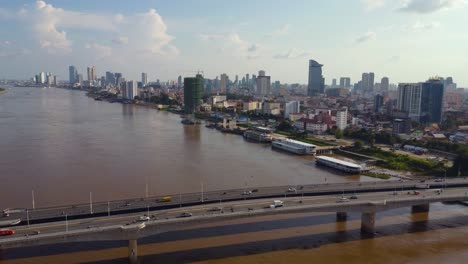 drone view of cars passing over bridge over the river, city in the distance