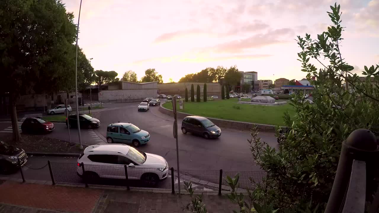 Timelapse from day to night of traffic in a big roundabout during a working day with a cloudy sky but visible sun
