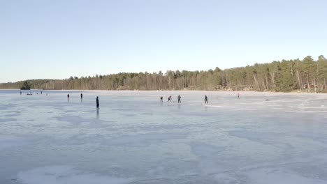 a group of people playing ice hockey on a large frozen lake surrounded by tall green trees