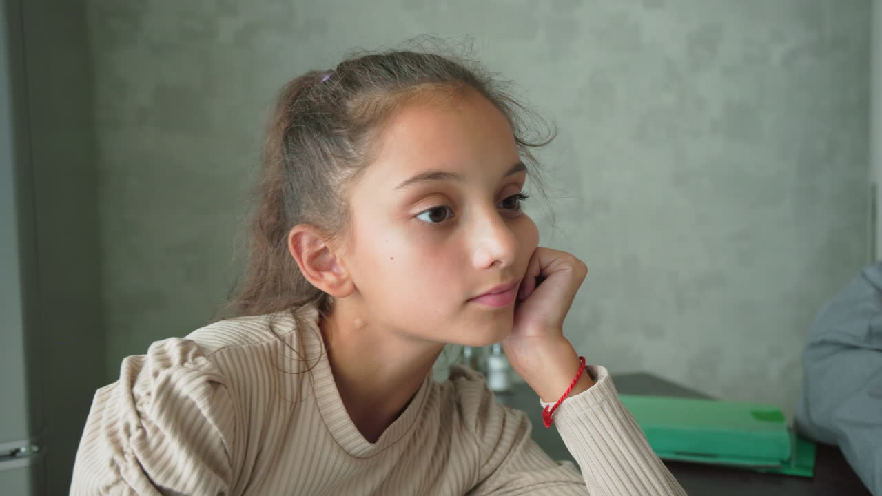 Sad girl and frustrated boy sitting apart at table with green folders and brown book in quiet modern room, both looking away in silence, showing emotional disconnection, boredom, and academic pressure