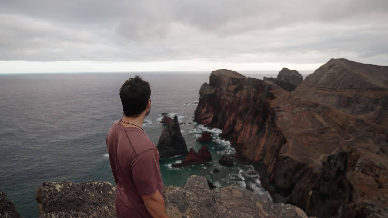 A man stands on a cliff edge at Ponta de São Lourenço, gazing out at the rugged coastline under moody skies.