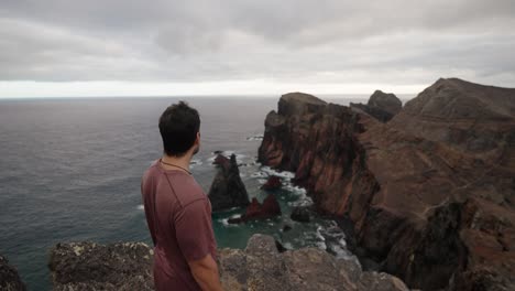 a man stands on a cliff edge at ponta de são lourenço, gazing out at the rugged coastline under moody skies.