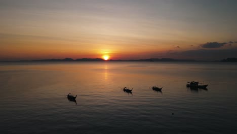 beautiful sunset over the dark silhouettes of an island, while traditional thai boats are quietly floating in the foreground