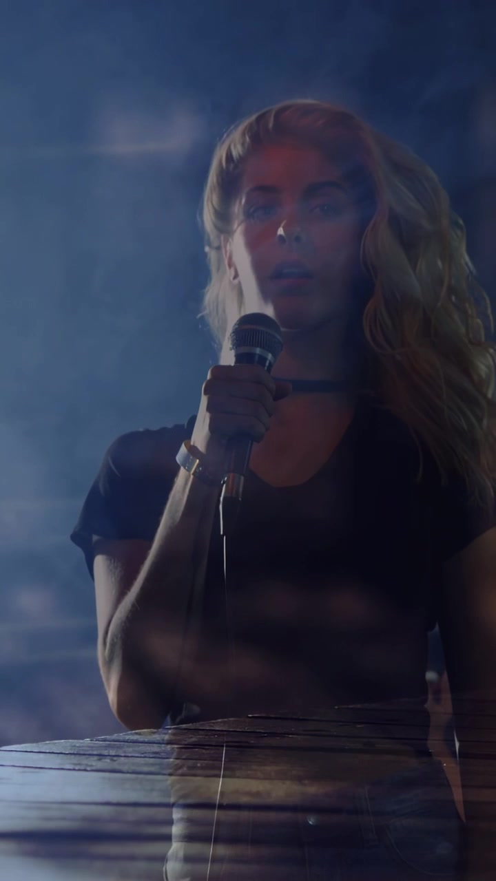 Vertical video: Female singer on music cue, holding mic, tilting back to front under blue overlay