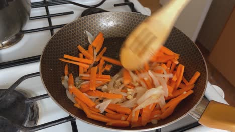 carrots and julienned onions are sautéed in a pan