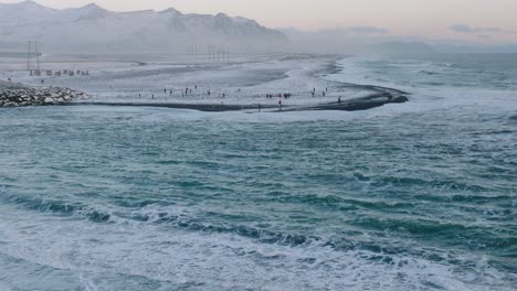 Aerial-landscape-view-over-people-on-the-shoreline-of-diamond-beach,-covered-in-snow,-at-sunset