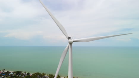 Green-Energy-Production,-Wind-Mill-Turbine-near-the-Coastal-Sea-with-Clouds-and-a-Blue-Sky,-Aerial-View