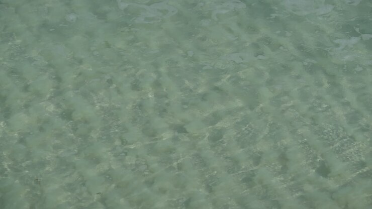 Super clear water wave rolling onto shore, ripple pattern in sand