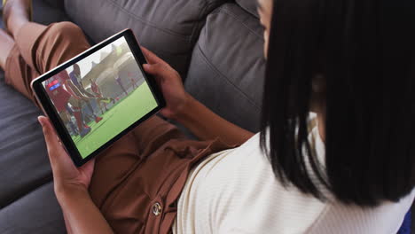 compuesto de una mujer sentada en casa en el sofá viendo un partido de hockey en la tableta