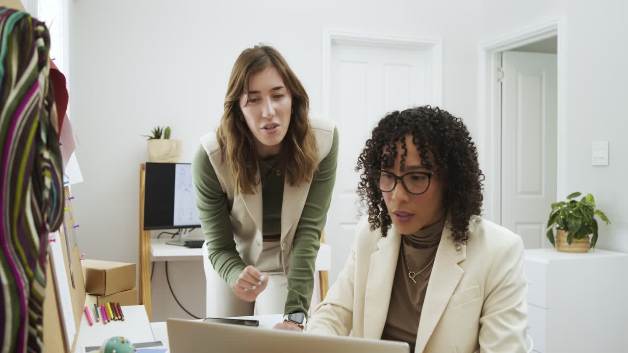 With pen-toting coworker entering diverse female coworkers reviewing laptop and board in office