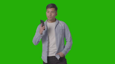 studio shot of casually dressed young man talking on mobile phone against green screen 1