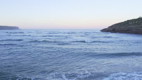 Cantabrian-sea-tide-enters-secluded-Playa-de-la-Arena-sunset-glow-LOW-AERIAL