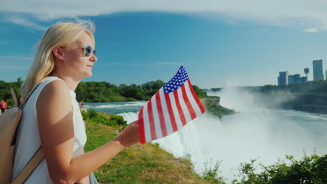 traveling in the usa - a woman with the flag of america in her hand admires niagara falls one of the