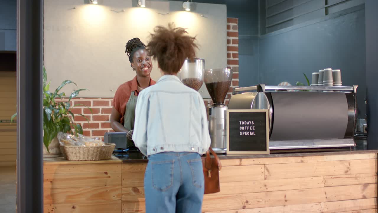 Donne afroamericane al bancone; una cliente si avvicina, prende la borsa e ordina, mentre il barista utilizza il POS.