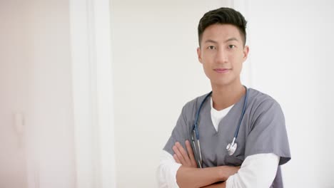 Portrait-of-happy-biracial-male-doctor-against-white-wall-with-copy-space,-slow-motion