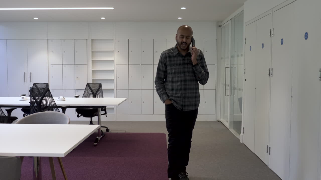 un empleado asiático paseando de un lado a otro mientras habla por su teléfono móvil discutiendo negocios en un entorno de oficina vacío