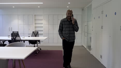 an asian male employee pacing up and down while talking on his mobile phone discussing business in an empty office environment