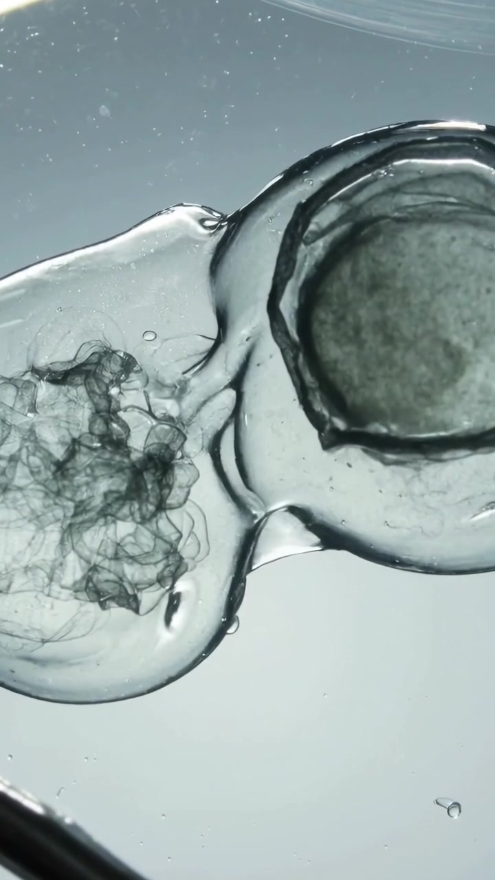 Video verticale: Gocce che si uniscono mentre la sfera sinistra sale su un piatto illuminato, fibre che si muovono, sonda nelle vicinanze