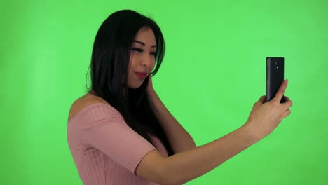 young attractive asian woman photographs with smartphone (selfie) - green screen studio
