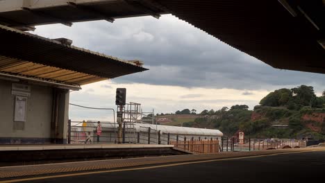 Der-Zug-Fährt-Aus-Dem-Bahnhof-Dawlish,-Devon,-Großbritannien,-Unter-Einem-Grauen-Himmel