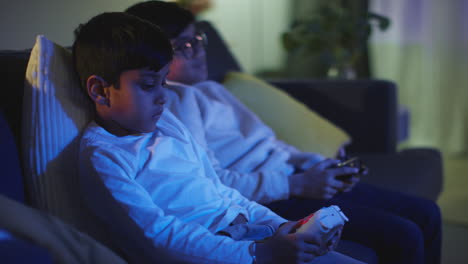 side view of two young boys at home having fun playing with computer games console on tv holding controllers late at night 1