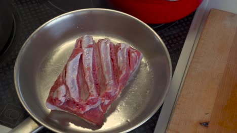 Top-down-view-of-pork-belly-being-placed-in-stainless-steel-pan-with-tongs