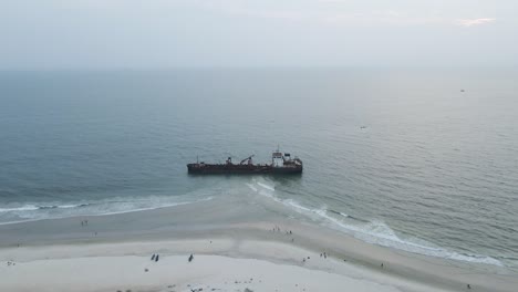 Luftaufnahme-Von-Touristen,-Die-Alte-Rostige-Wracks-Am-Sandstrand-Mit-Meer-Im-Hintergrund-Besuchen