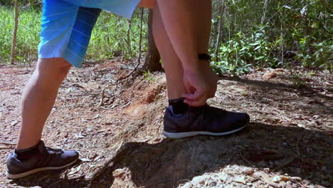 el hombre se detiene para atarse los zapatos mientras camina por el monte