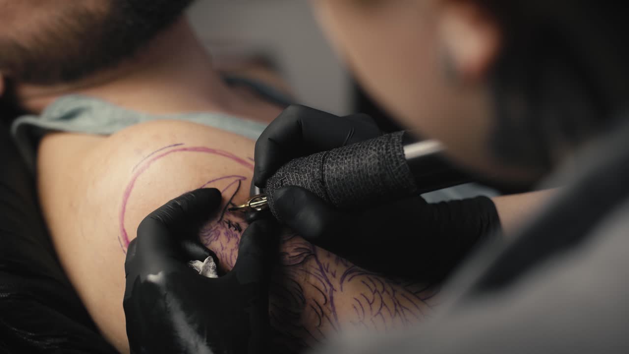 Primo piano di una tatuatrice che tatua le braccia del suo cliente.