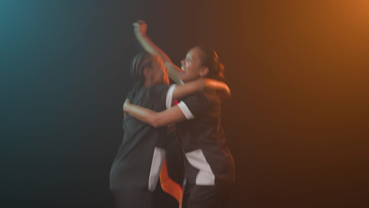 Compagne di squadra afroamericane con divise abbinate che alzano una bandiera abbracciandosi per celebrare la vittoria in studio.