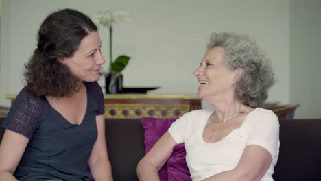 Smiling-middle-aged-daughter-and-mother-talking-on-sofa