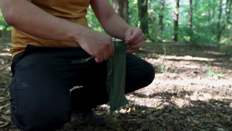 tourist put tent anchors in a bag, tie it and prepare to leave the forest campsite