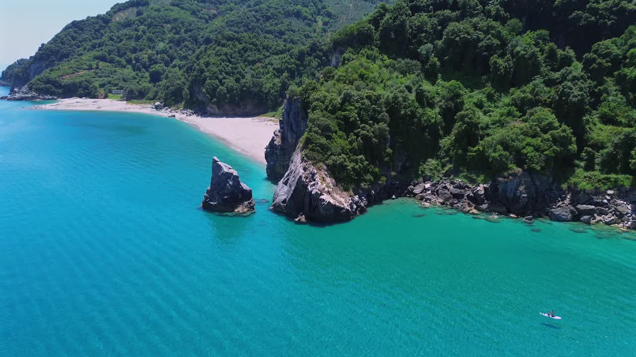 Ripresa cinematografica con drone in orbita e allontanamento che rivela le iconiche formazioni rocciose e le rigogliose scogliere verdi della spiaggia di Agii Saranta. Veduta dall'alto delle acque turchesi del Mar Egeo a Pelio, Grecia. Nessun audio.