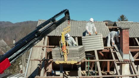 construction workers in ppe and hard hats dismantling roof tiles of a demolished house on a sunny day. drone sideways