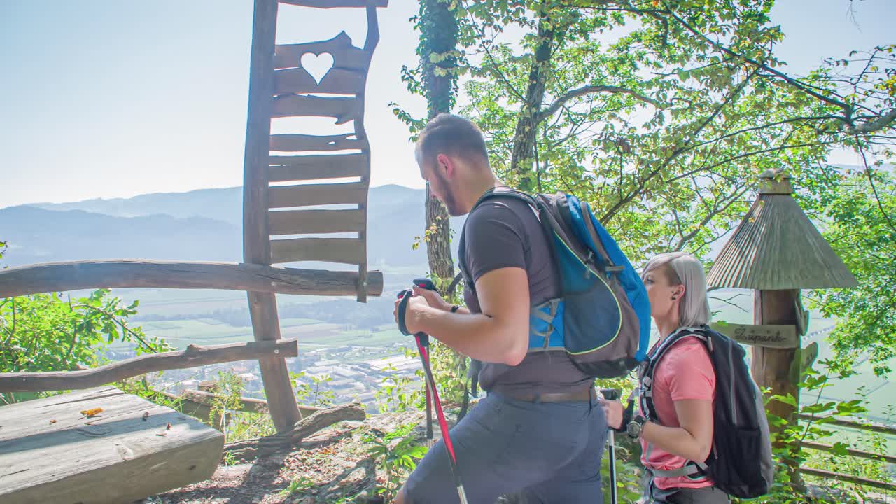 Man and woman walk up to a lookout point on top of the hill. Follow shot. Green window, Slovenia
