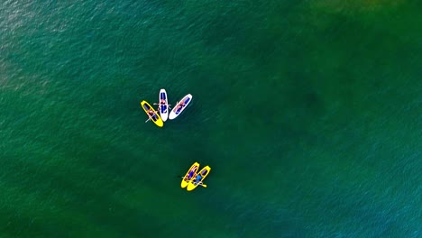 un grupo de amigos conversan entre ellos mientras se sientan en tablas de remo en el agua