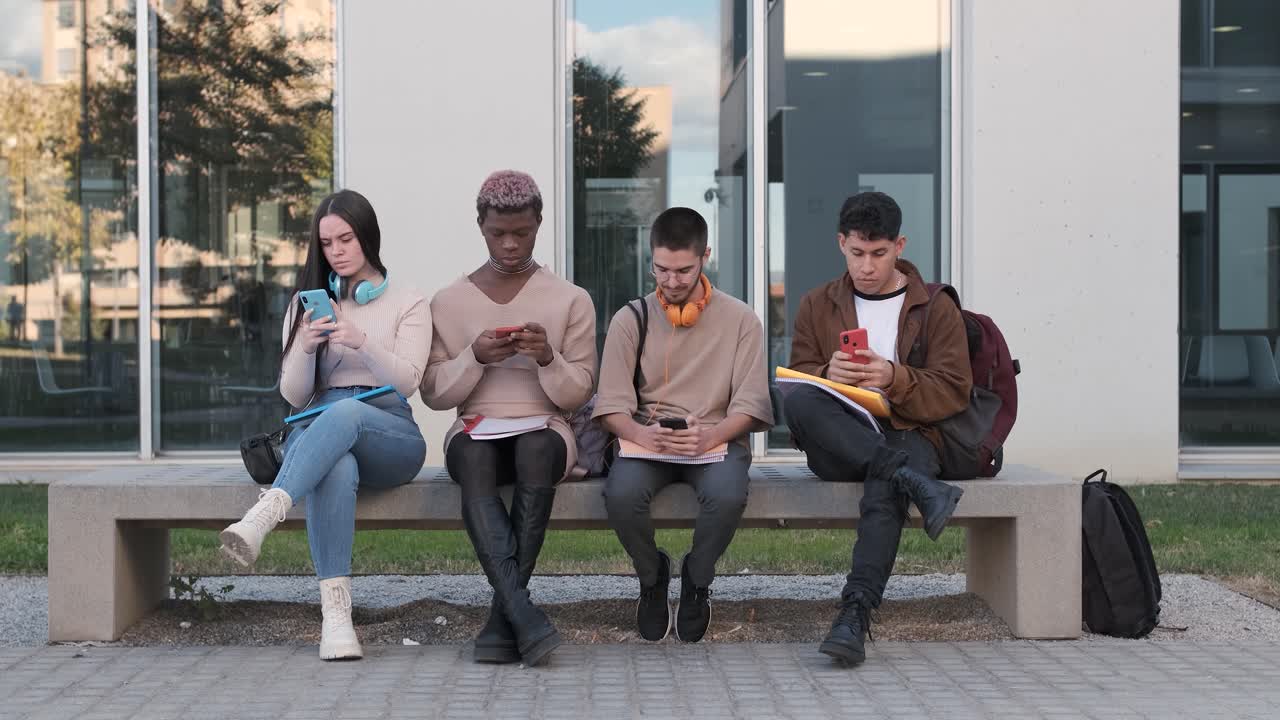 Multiethnic friends sitting on a bench using mobiles