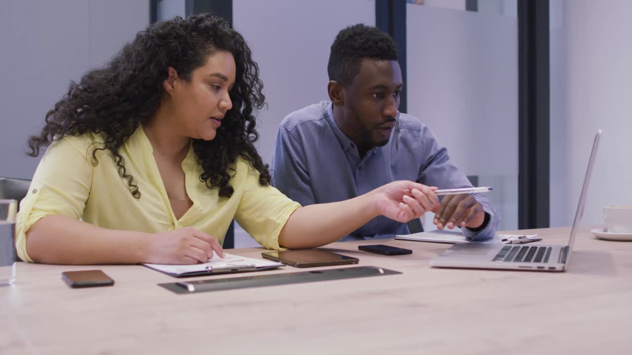 Focused diverse couple of business people working together, using laptop in modern office