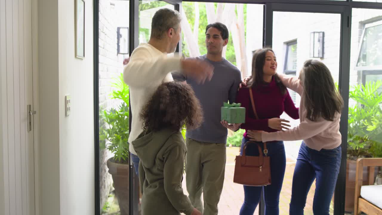Mature couple opening glass double doors at entryway and welcoming arriving family with gift box