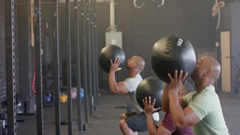 diverse male group fitness class training at gym lifting and throwing medicine balls, in slow motion