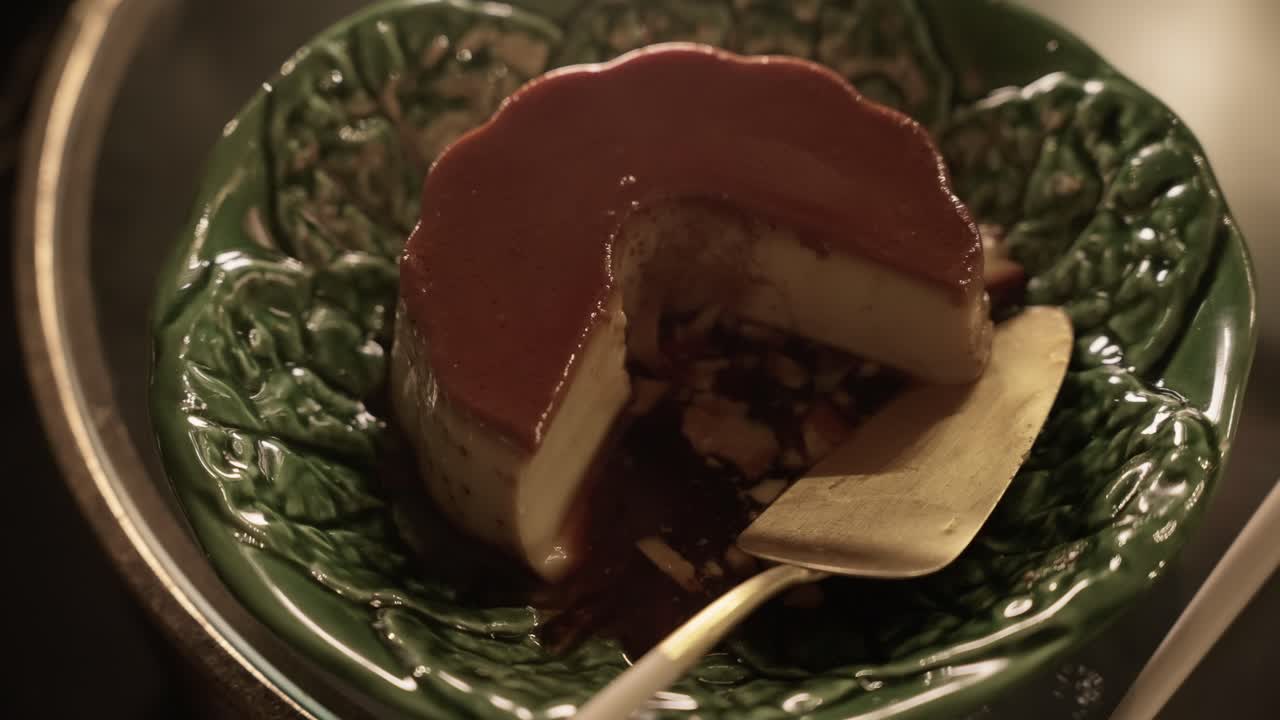 close up of sliced caramel flan with rich sauce in green ceramic leaf shaped bowl