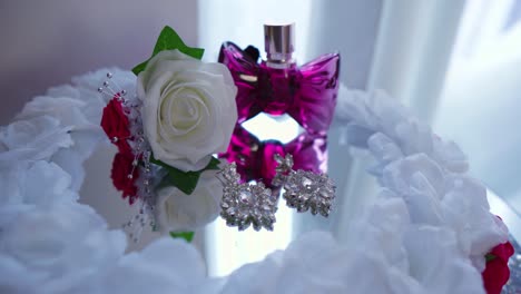 Luxury-white-rose-and-purple-perfume-in-shape-of-bow-placed-on-a-mirrored-table-reflecting-surrounded-by-clouds-like-decoration-in-white-room-natural-light-gypsy-wedding-roma-people-tradition-cinema