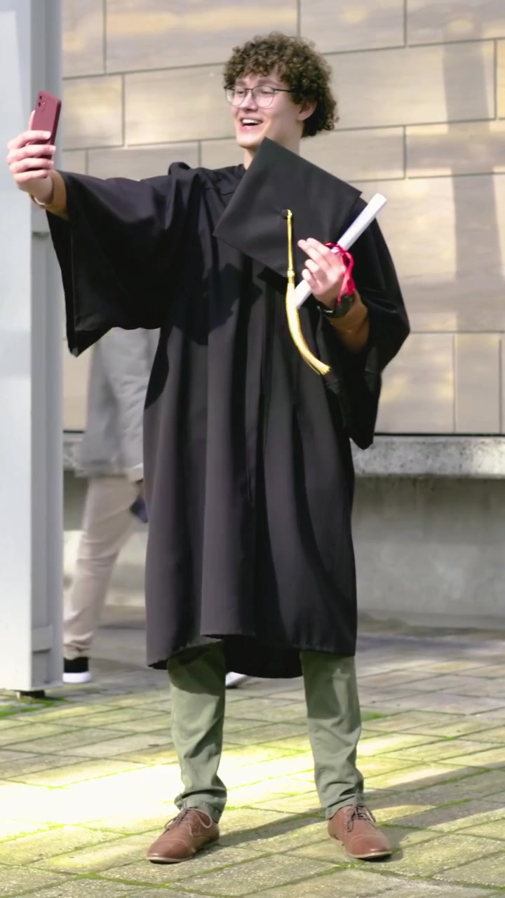 Video verticale: Laureato al centro in toga solleva il telefono posando per un selfie in piazza con il diploma.
