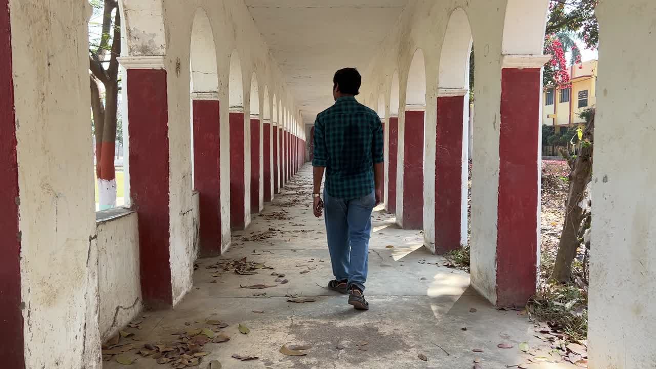 Rear view of a man walking through corridor with arched opening son both sides in India.