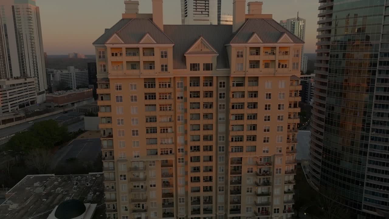 Aerial of apartment building in golden evening light, surrounded by modern skyscrapers in Buckhead, Atlanta, Georgia. The urban landscape highlights contemporary architecture, real estate growth