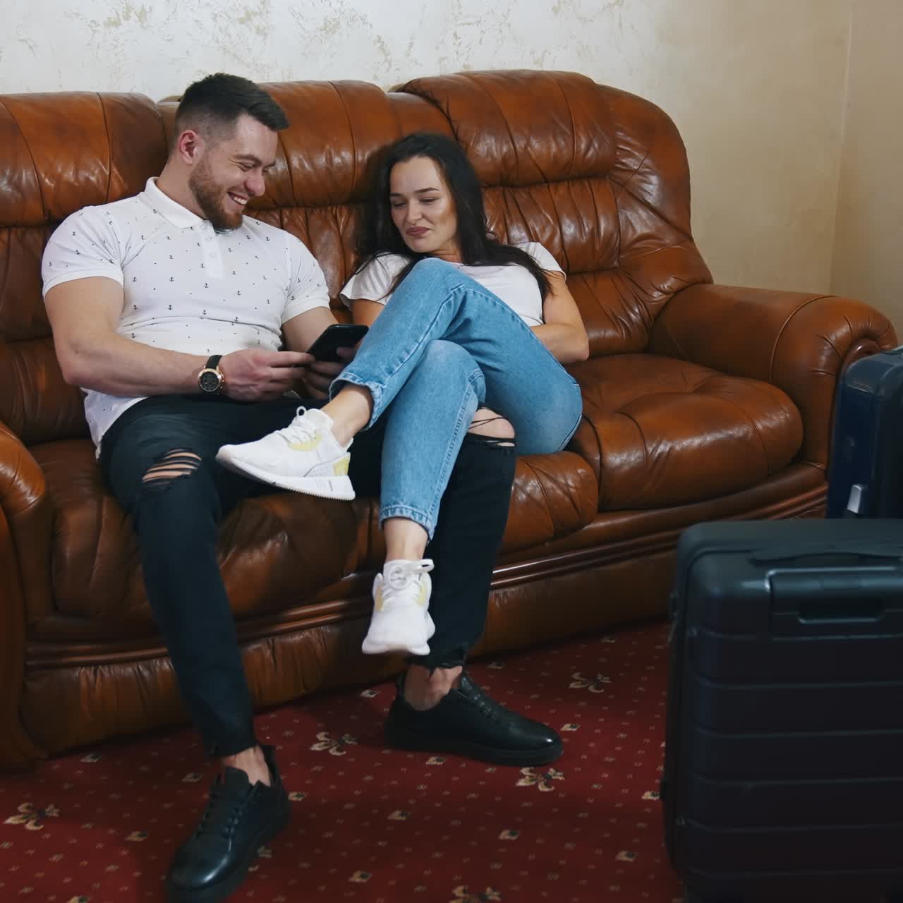 Couple on couch near packed suitcases. Young man and woman resting on a sofa after a long journey in a hotel. Happy couple in love waiting for the departure