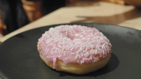 las manos de un niño sosteniendo una rosquilla rosa con salpicaduras blancas