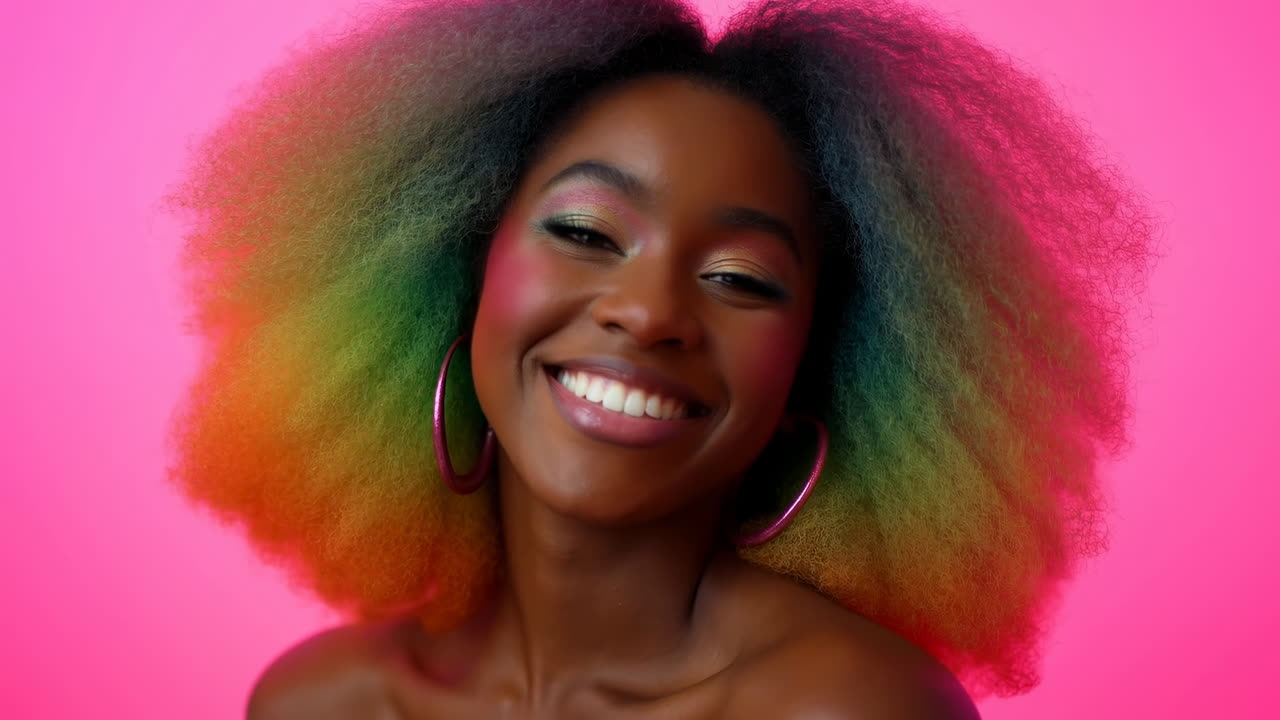 Donna sorridente con capelli afro colorati su sfondo rosa, orecchini a cerchio, trucco vivace, spalle scoperte
